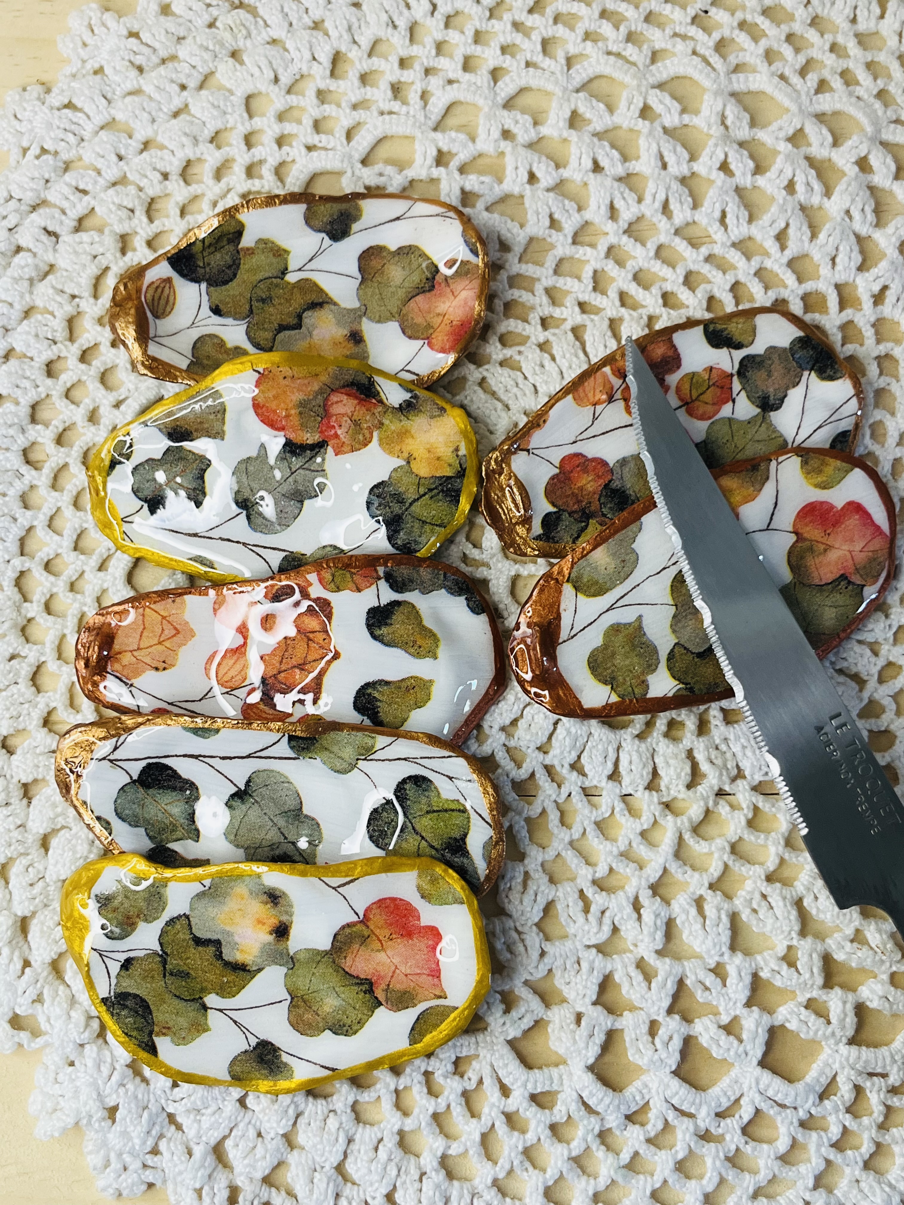 Invitez la chaleur et la douceur de l’automne à votre table grâce à ces porte-couteaux uniques, sublimés à la main. Chaque coquille, soigneusement sélectionnée, révèle un décor de feuillages colorés aux tons chauds : ocres, dorés, rouges profonds et bruns cuivrés.